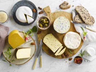 kaasschotel met hartige zuiderse toets Kaasschotel op marmeren keukenblad. Verschillende Belgische kazen liggen op houten planken met brood, noten, radijzen en chutney erbij.