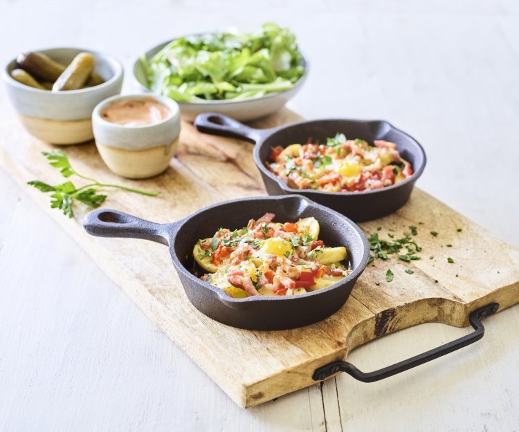 Twee gourmetpannetjes staan te sieren op een houten snijplank. Als bijgerechtjes hebben we een groene salade, opgelegde augurkjes en een cocktailsausje.