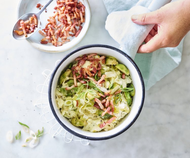 Aardappelpuree met spruitjes en spekjes Smeuïge aardappelpuree met grofgehakte spruitjes en prei klaargemaakt in een kookpot. De kok in kwestie voegt de versneden lente-uitjes en gebakken spekjes toe als afwerking.