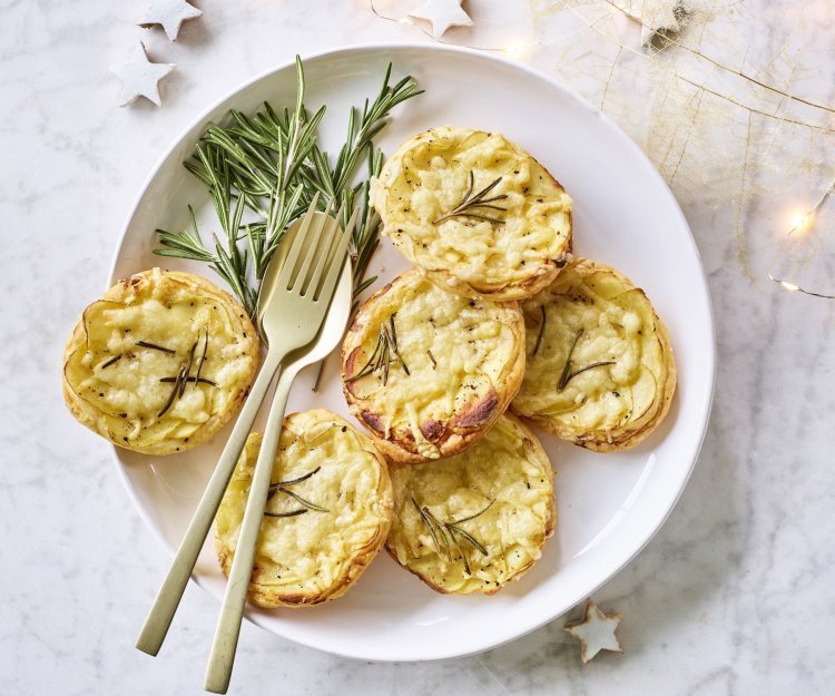 Aardappeltaart met bladerdeeg en Flandrien kaas Taartjes met schijfjes aardappel en Belgische kaas liggen op een wit bord. Goud gestek ligt op het bord om meteen zo'n taartje op te scheppen. Er liggen enkele sterretjes en lichtjes langs om de feesttafel extra te laten blinken.