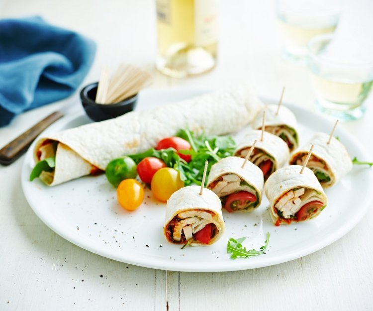 Op een bord ligt een rol wrap met groenten, wat kerstomaten en zes stukken wrap met een prikker in. Op een bord ligt een rol wrap met groenten, wat kerstomaten en zes stukken wrap met een prikker in.