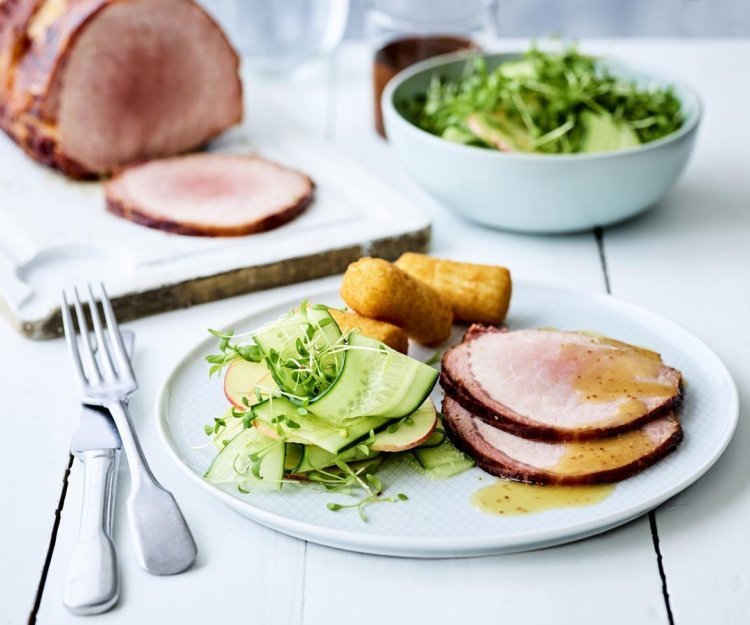 Ardeens gebraad met mosterdsaus, oude Geuze en een salade van appel en komkommer Op een houten witte tafel staat een portie klaar. Een wit bord gevuld met twee sneetjes van het varkensgebraad, kroketten en de salade van komkommer met appel.