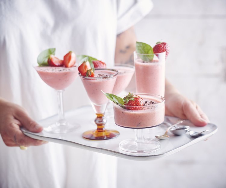 Bavarois van aardbei met basilicum en zwarte peper Roze bavarois geserveerd in verschillende glaasjes op een dienplateau. Een vrouw met witte t-shirt draagt deze roze dessertjes, klaar om naar de gasten te brengen.