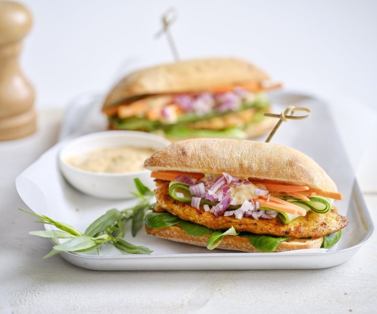 Belegd broodje met gegrilde kip Een belegd broodje ligt op een bordje. Hij is belegd met een stukje gebakken kipfilet, verse wortel, komkommer en een sausje. De resterende saus werd in een klein potje erbij geserveerd.