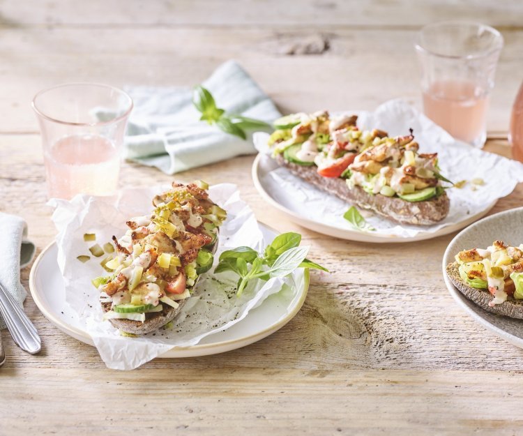 Er staan 3 bordjes klaar op een houten tafel. De ideale lunch om te benuttigen buiten in de zon. De halve broodjes zijn belegd met kruidige kip en verse groentjes. 