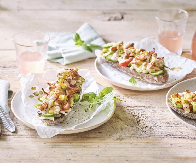 Belegd broodje met kruidige kip Er staan 3 bordjes klaar op een houten tafel. De ideale lunch om te benuttigen buiten in de zon. De halve broodjes zijn belegd met kruidige kip en verse groentjes.