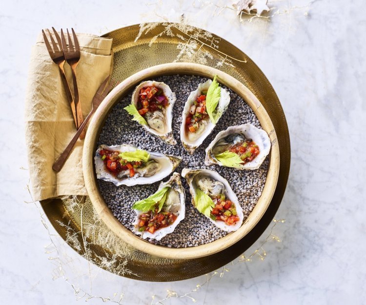Bloody Mary oesters Zes oesters liggen te schitteren op de feesttafel. Ze zijn voor de helft gevuld met de vinaigrette op basis van tomatensap, stukjes paprika's en vodka. Afgewerkt met een blaadje selder die zorgt voor de frisgroene kleur bij de rode topping.