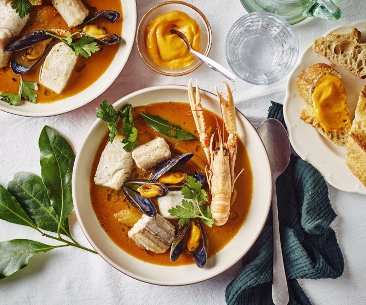 Bouillabaisse belgique Een heerlijk kleurrijk bordje bouillabaisse staat op tafel. Wij maakten hem met topproducten van hier. Er ligt een donker groene linnen servette langs en bordje stukjes brood en verse rouille.