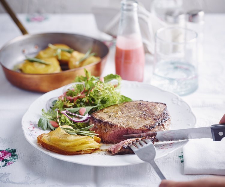 Chateaubriand met millefeuille van aardappelen en een kruidenslaatje met frambozendressing Een hoofdgerecht om U tegen te zeggen. We serveren een malse chateaubriand met millefeuille van aardappelschijfjes en knapperige kruidensalade. De frambozendressing staat langs het bord in een klein glazen flesje. Er staat ook een glas water boven het bord, naast peper en zout.