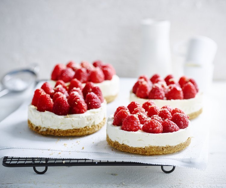 No bake-cheesecake met witte chocolade en frambozen Wij maakten 4 kleine cheesecakes en staan op een wit boterpapiertje. Ze zijn afgewerkt met verse frambozen die een mooi contast geven met het witte van de kaas.