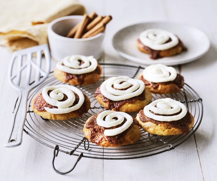 Cinnamon rolls-koekjes Op een taartrooster liggen 6 koekjes af te koelen. Het zijn koekjes van cinnamon rolls, een nieuwe versie om te genieten van deze heerlijke en kruidige zoetigheid. Op de koekjes is frosting gespoten op basis van roomkaas.