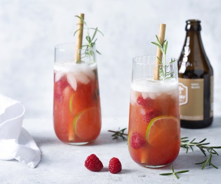Cocktail met wit bier en gin 2 cocktails staan uitgeschonken in grote glazen. Deze cocktail op basis van bier en gin werd afgewerkt met frambozen en rozemarijn.