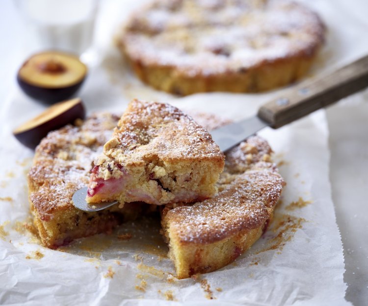 Crumble-taart met pruimen Er liggen twee crumbletaartjes klaargemaakt op het aanrecht. Er is al eentje aangesneden om meteen te proeven.