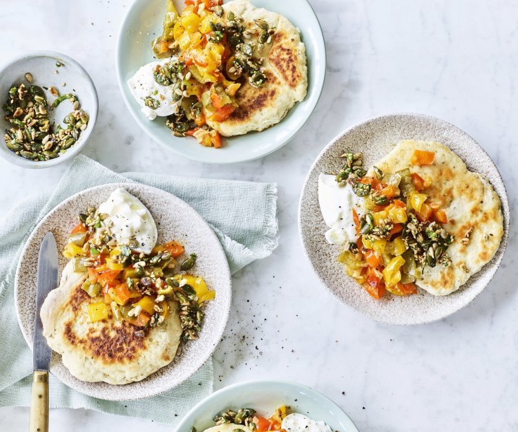 4 bordjes staan op tafel elk gevuld met een stukje flatbread, hier bovenop gestoofde paprikablokjes in 3 kleuren, een stukje burrata en zadencrumble. 