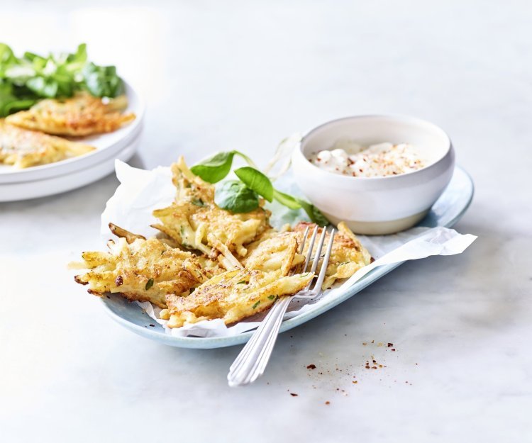 Meerdere fritters liggen op een licht blauw bordje vergezeld van een blaadje veldsla en het dipsausje op basis van yoghurt en specerijen.