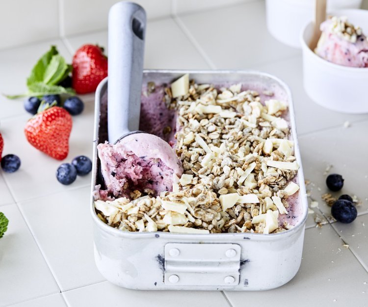 Frozen yoghurt met blauwe bessen en aardbeien Heerlijk yoghurtijs met blauwe bessen en aardbeien. Het ijs komt net uit de vriezer en zit in een box van inox, er is al een bolletje gerold met de ijsschep en ligt te wachten op een kandidaat. We voegden nog vers fruit en een topping van havermout en zonnebloempitten toe voor extra crunch.