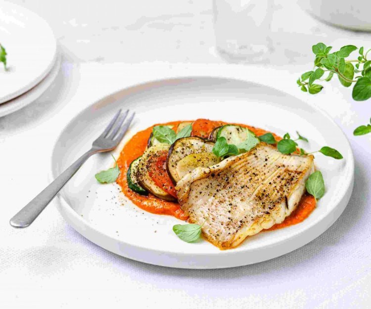Gebakken rog met ratatouille en paprikasaus Gebakken rog met ratatouille en paprikasaus geserveerd op een wit groot bord. Het vork ligt op het bord en verse kruiden staan langs deze hoofdmaaltijd.