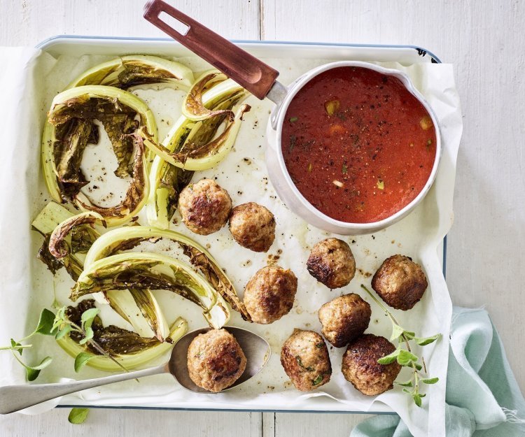 Gegrilde bloemkoolbladeren met balletjes en tomatensaus Gegrilde bloemkoolbladeren liggen op de ovenschaal met gehaktballetjes en tomatensaus in een sauspannetje.