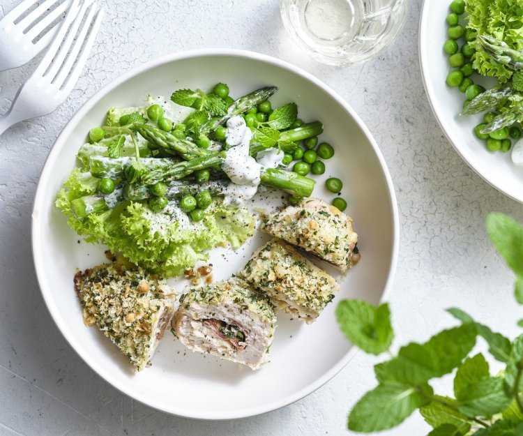 Gegrilde kipfilets met crumble en groene salade Hier wil ik meteen aan beginnen. De kipfilet is gevuld met basilicum, plakje kaas en ham. Daarna kreeg hij een flinke laag pako over zich heen en ging hij de oven in. Wij combineren deze krokante gegrilde kipfilet met een groene salade op basis van krulsla, erwtjes, groene asperges en verse munt. Dit gerechtje is opgediend in een wit bord om de groene kleur extra pit te geven.