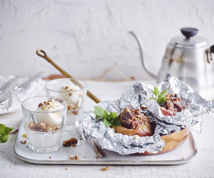 Gepofte appel met crumble van speculoos en vanilleijs Een vers gepofte appel vanop de bbq ligt in een klein pannetje op een dienblad vergezeld met een glaasje vanilleijs en verse koffie.