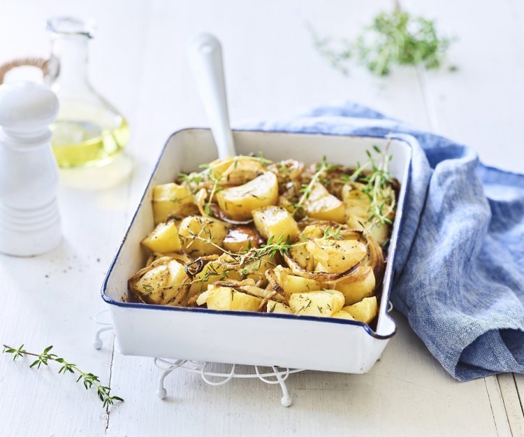 Geroosterde aardappelen met balsamico Een witte ovenschaal met donkerblauw randje staat op een keukenonderlegger op een witte houten tafel. Er staat een witte pepermolen en een glazen flesje met olijfolie langs. De verse tijm zorgt voor extra kleur bij de geroosterde aardappelen, er ligt ook nog een blauwe linnen servette langs de ovenschotel.