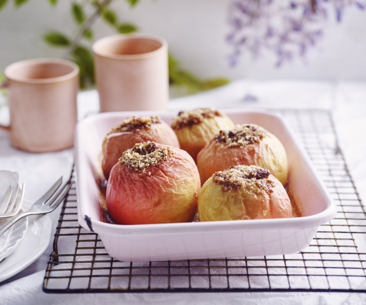 Gevulde appels in een licht roze ovenschaal. Achteraan staan twee roze kopjes, klaar om aan het ontbijt te beginnen.