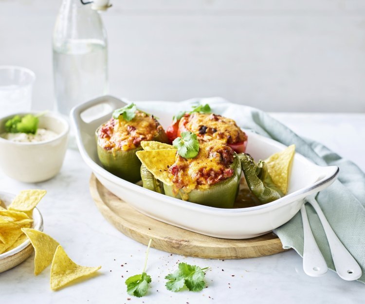 Een witte ovenschaal staat op tafel te blinken met opgevulde groene paprika's. Ze zijn gevuld met chili con carne en enkele nacho's. Dit is sowieso een gerechtje dat jong en oud niet koud laat. 