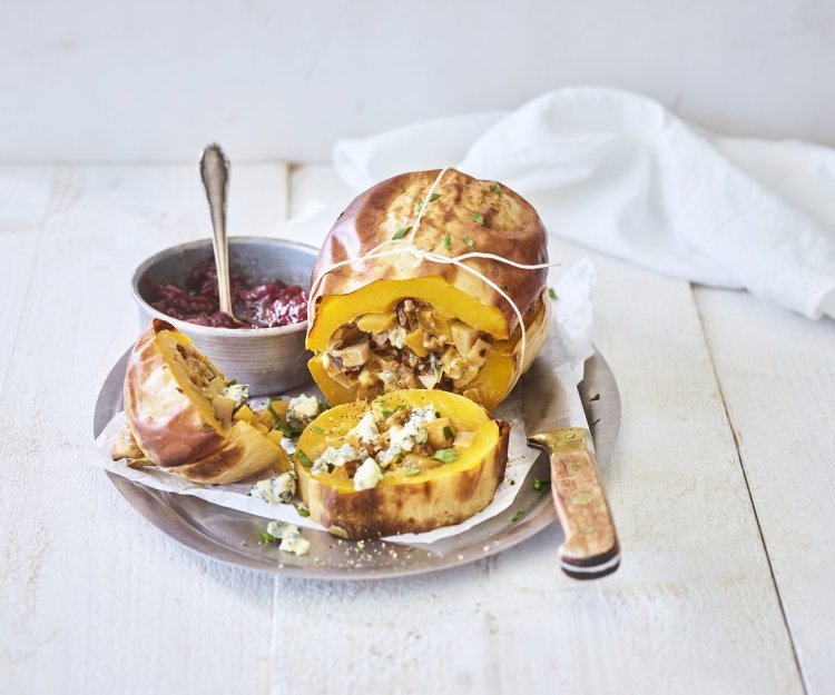 Gevulde pompoen met aardappel, prei en blauwe kaas Een butternut-pompoen ligt op een schaal van inox. Hij is mooi opgevuld met een mengsel van krieltjes, preistukjes en blauweschimmelkaas. Wij combineren hem met veenbessencompote om een zoete smaak toe te voegen.