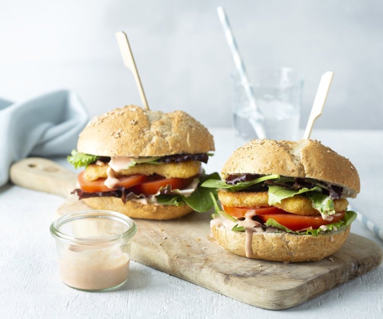 Hamburger met berloumi Een heerlijke hamburger die niemand koud laat. We maakten hem extra crunchy door de kaas te paneren alvorens hem te bakken. De twee hamburgers liggen op een houten snijplank met een prikker middendoor.