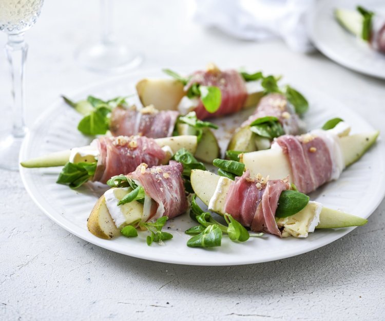 Hapje van peer, Ganda, brie en walnoot Op groot wit bord ligt het hapje geserveerd, de partjes peer met een stukje brie omwikkeld met een sneetje gandaham. Simpel gerechtje, boordevol smaak en kleuren. De groene verse waterkers maakt het volledig af.