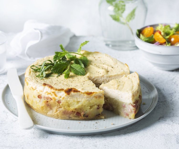 Hartige cheesecake met puree en tomatenslaatje Een hartige cheesecake smaakt heerlijk als lunch of avondmaal. Door het tomatenslaatje krijg je de frisse toets die de cheesesmaak verfrissen. De cheescake ligt aangesneden op een groot rond bord, het slaatje staat langs het bord en een karaf water met takje munt zie je achteraan in de foto.