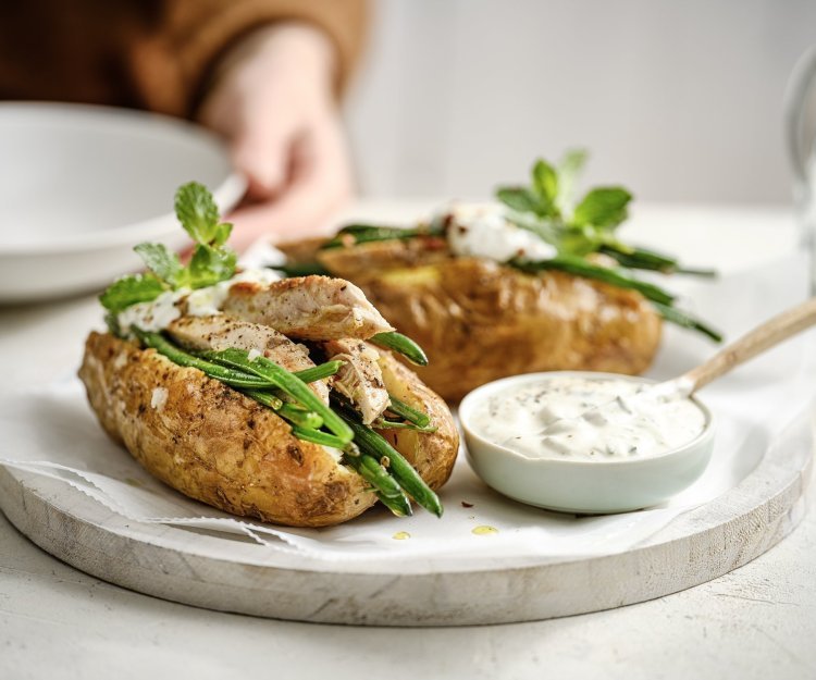 Twee gepofte aardappelen liggen op een plateautje, ze zijn gevuld met 