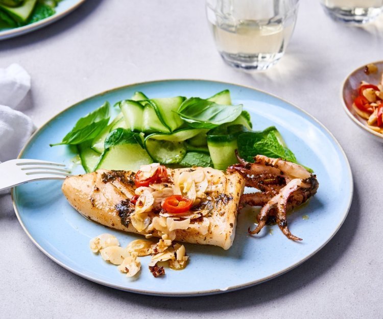 Inktvis met crunchy amandelen en slaatje van komkommer en kruiden Op een lichtblauw bordje ligt een gegrilde inktvis met amandelen te blinken. Wij serveren hem met een slaatje op basis van komkommer, munt en basilicum.