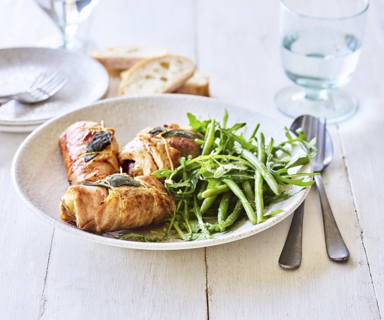 Involtini met peer en geitenkaas Heerlijke kalfsrolletjes liggen in een diep bord met de boontjessalade er naast. De vleesrolletjes zijn gevuld met peer en geitenkaas. Er staat een glas water langs en wat stukjes brood.