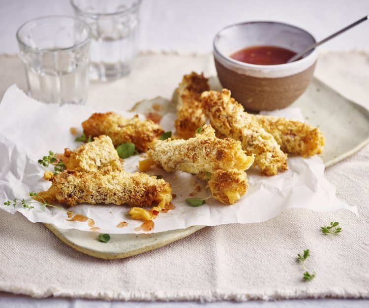 Kaassticks van Brugge Oud kaas met rauwe ham Krokante kaaskroketten liggen op een dienchaaltje, met een dipsausje in een zelfgedraaid keremakiekpotje. Er staan twee glaasjes water naast en de sticks zijn afgewerkt met verse oregano.