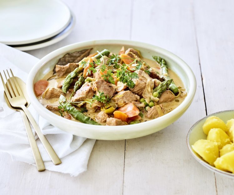 Kalfsfricassee met lentegroenten Deze fricassee straalt een en al lente uit! Hij is klaargemaakt met jonge worteltjes, erwtjes en aspergepunten. Er ligt gouden bestek langs en een portie gekookte aardappelen.