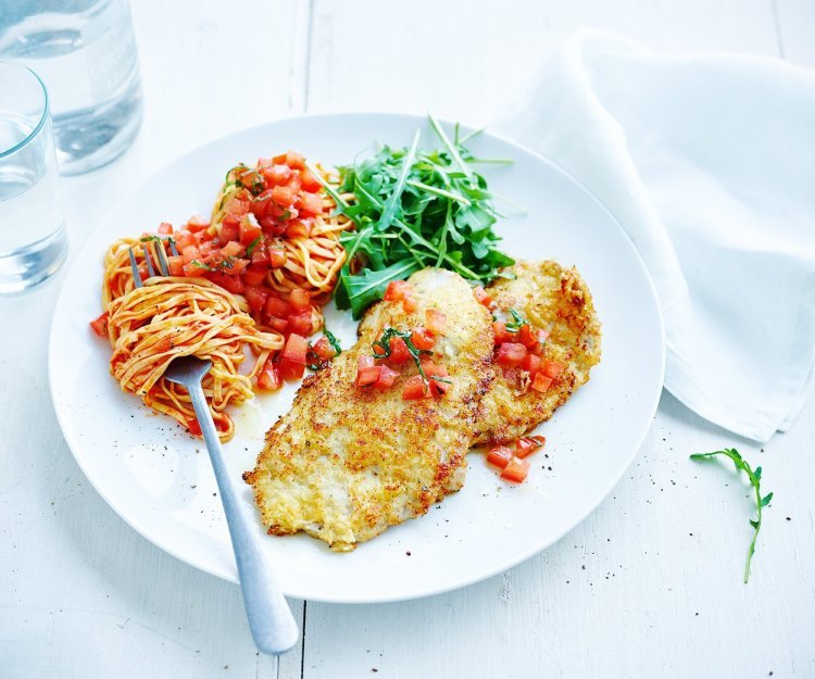 Kalfslapjes alla Milanese met tomatensalsa Op tafel staat een portie van de krokante kalfslapjes alla Milanese met tomatensalsa, pasta en rucola.