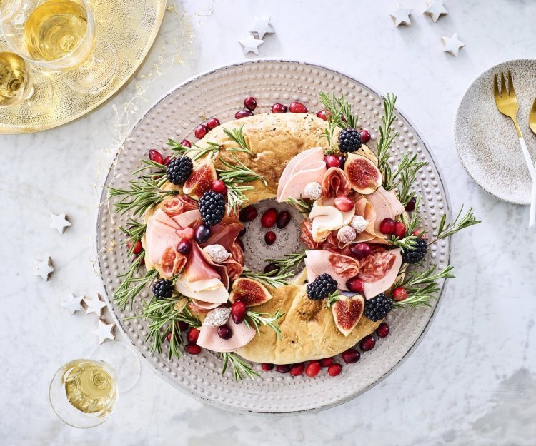 Kerstkrans met charcuterie Een echte Kerstkrans om op te eten. De krans is gemaakt van een Turks brood die belegd werd met verschillende vleesjes, fruit en rozemarijn. Hij staat op de feesttafel en enkele zilveren sterren liggen er langs vergezeld met enkele aperitiefjes.