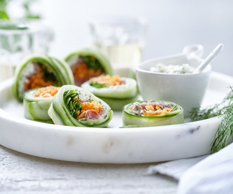 Rolletjes van komkommer gevuld met cottage cheese, wortel, rucola en rosbief. Een heerlijke gezonde en kleurrijke snack op een bordje van marmer. De overige mengeling met de cheese is geserveerd in een dippotje om eventueel een extra toefje te nemen. 