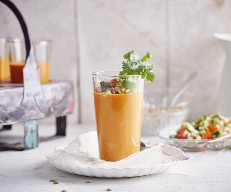 Een gazpacho van paprika geserveerd in een groot glas zorgt intens voor een feestlook. Deze koude soep werd gepimpt met stukjes komkommer en tomaat, als afwerking nog enkele blaadjes koriander en zonnebloempitten bovenop. 