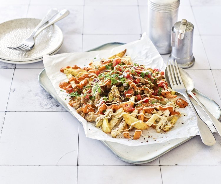 Loaded fries van aardappel, zoete aardappel en knolselder met kip en paprika Op het aanrecht ligt een serveerschaal met een wit bakpapiertje op. Hierop liggen geroosterde aardappel, zoete aardappel en knolselder. Hierop strooien we paprika, gehakt en een sausje. Er staan bordjes langs om op te scheppen en aan te vallen.