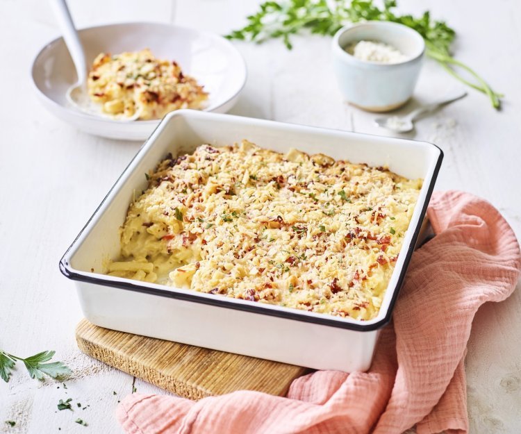 Een heerlijke gevulde ovenschotel boordevol comfortfood staat op de tafel te blinken. Onze mac and cheese met Belgische kazen zit in een witte ovenschotel met donker blauw randje, zoals bij de bomma. Er ligt een zalmroze servette langs en de een takje verse peterselie voor extra kleur in het beeld. 