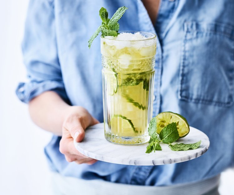 Mocktail met Jupiler 0.0 en peach ice tea Een heerlijk frisse mocktail van Jupiler 0.0 en peach ice tea. Geserveerd met frisse limoenschijfjes in het glas. De vrouw draagt een blauw jeanshemd en staat mee in beeld.