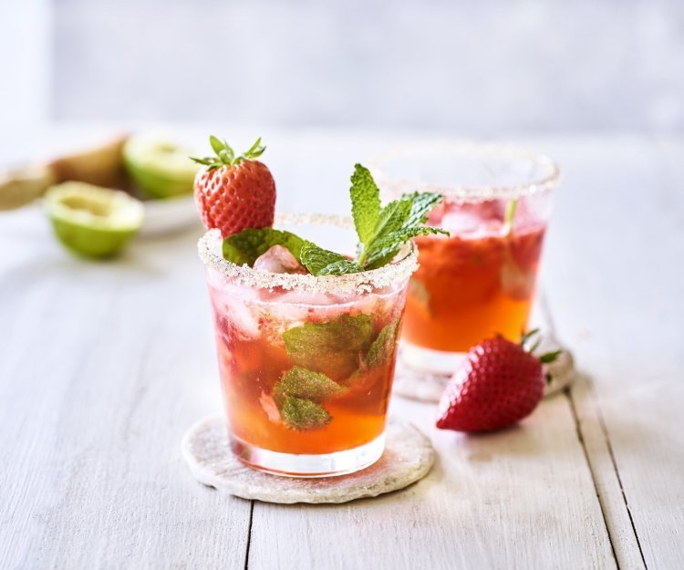 Mojito van aardbeien Twee roodgekleurde mojito's op de tafel, afgewerkt met verse munt en nog een aardbei. Alleen al kijken is een feestje, tijd om die cocktail te benuttigen. Het glad kreeg zelfs een suikerrandje.