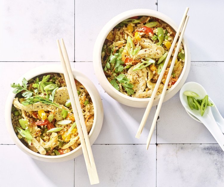 Nasi goreng van bloemkoolrijst met paprika, erwtjes en kip Twee kommetjes staan op het aanrecht. Wij maakten een op-en-top Belgische variant op de Nasi goreng, nl eentje met bloemkoolrijst, paprika, erwtjes en kip van bij ons.