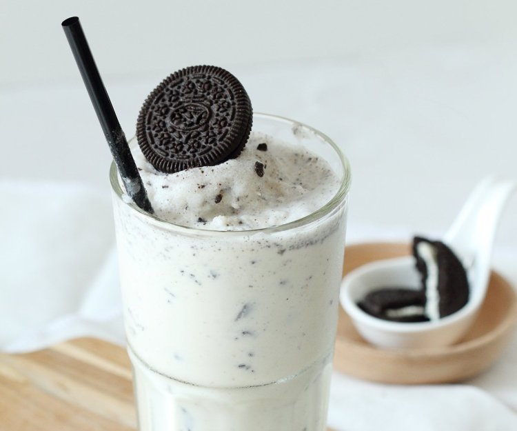In een groot glas zit onze huisgemaakte milkshake van melk met oreokoekjes. Hij heeft dus een witte kleur met zwarte stipjes. Hij is afgewerkt met een volledig koekje aan de rand van het glas. Oreo-milkshake