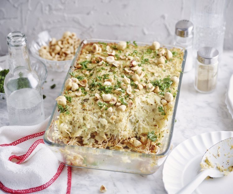 De ovenschotel met pulled chicken en knolselderpuree staat op tafel, hij is afgewerkt met hazelnoten en peterselie wat een mooie kleur geeft. Er ligt een lepel langs op een klein bordje om meteen uit te scheppen en met het hele gezin aan tafel te gaan.