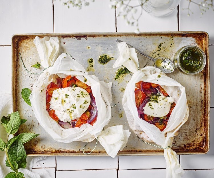Papillot van groenten met burrata en muntolie Twee papillotten liggen op een ovenplaat. De papillot is gemaakt in een wit boterpapiertje waarin de groenten een mooi contrast in geven. Denk maar aan de rode paprika's en tomaten. De burrata ligt er bovenop en de muntolie staat in een bokaaltje naast de papillotten.