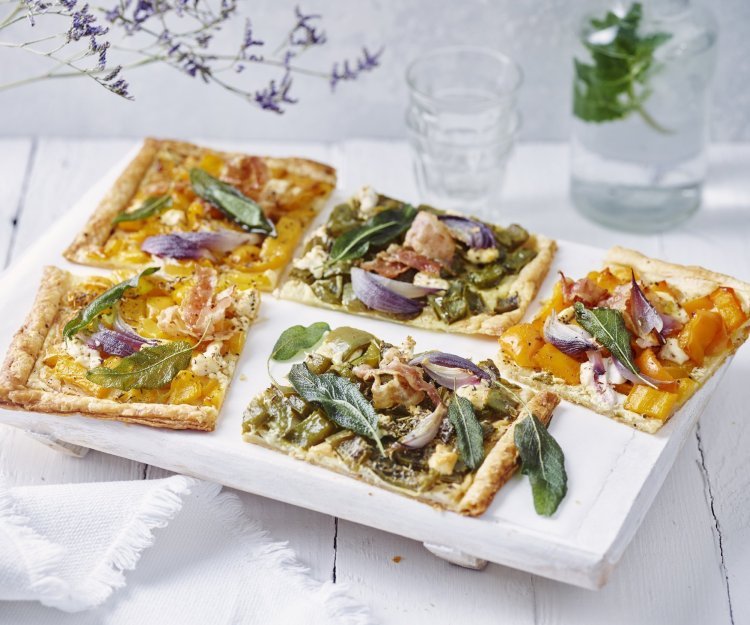 Plaattaart met paprika, spek en salie Plaattaart met paprika, spek en salie ligt aangesneden klaar op tafel. Er staat een fles water met glaasje langs. Paarse bloemen zorgen voor een extra toets in het beeld.