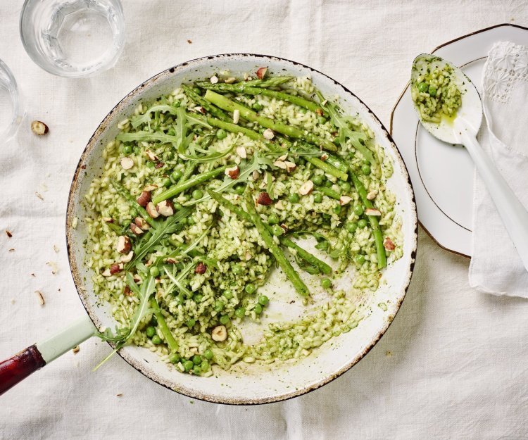 Risotto met hazelnootpesto, erwtjes en groene asperges De pan op tafel en scheppen maar. De risotto heeft een mooie groene kleur door de huisgemaakte pesto. We serveren hem met een portie extra groene groentjes zoals erwtjes, groene apserges en rucola.